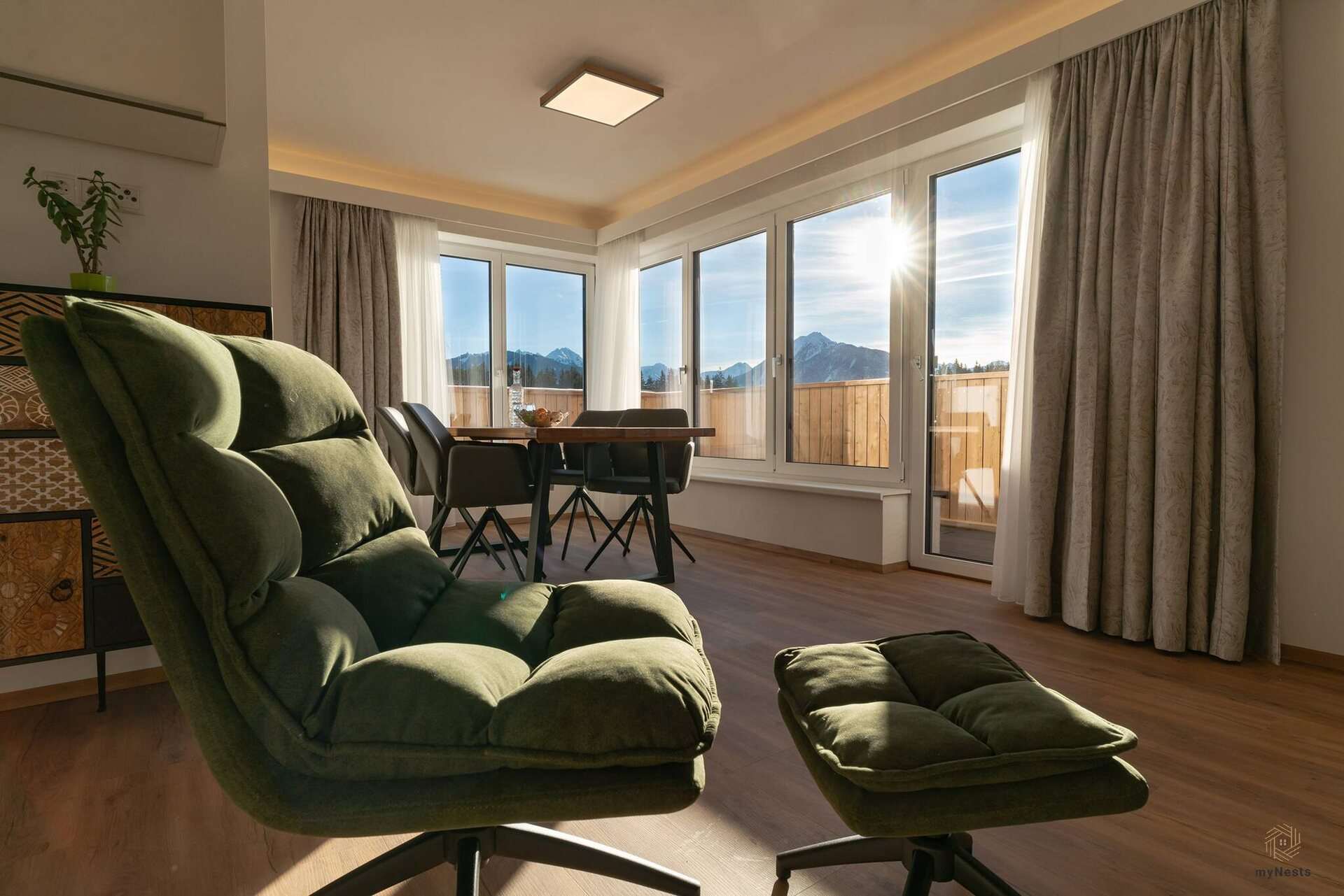 Zelené relaxační křeslo s podnožkou před jídelním koutem v apartmánu Bachstelze 10