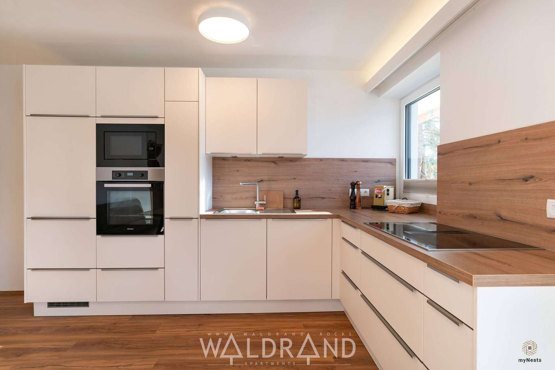 Weiße Küche mit Einbaugeräten und Holzrückwand im Apartment Kuckuck 7