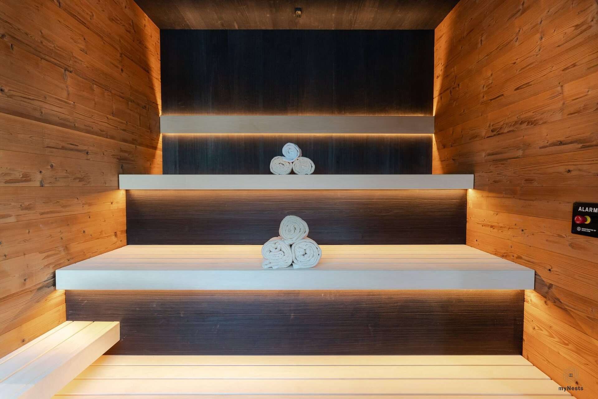 Sauna s nepřímo osvětlenými dřevěnými lavicemi a srolovanými ručníky
